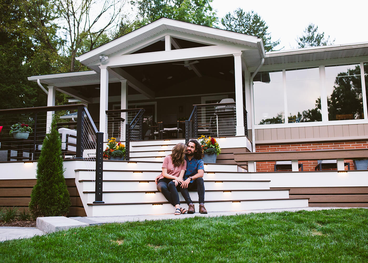 A young couple sitting on the steps of a modern composite deck design with steel railings